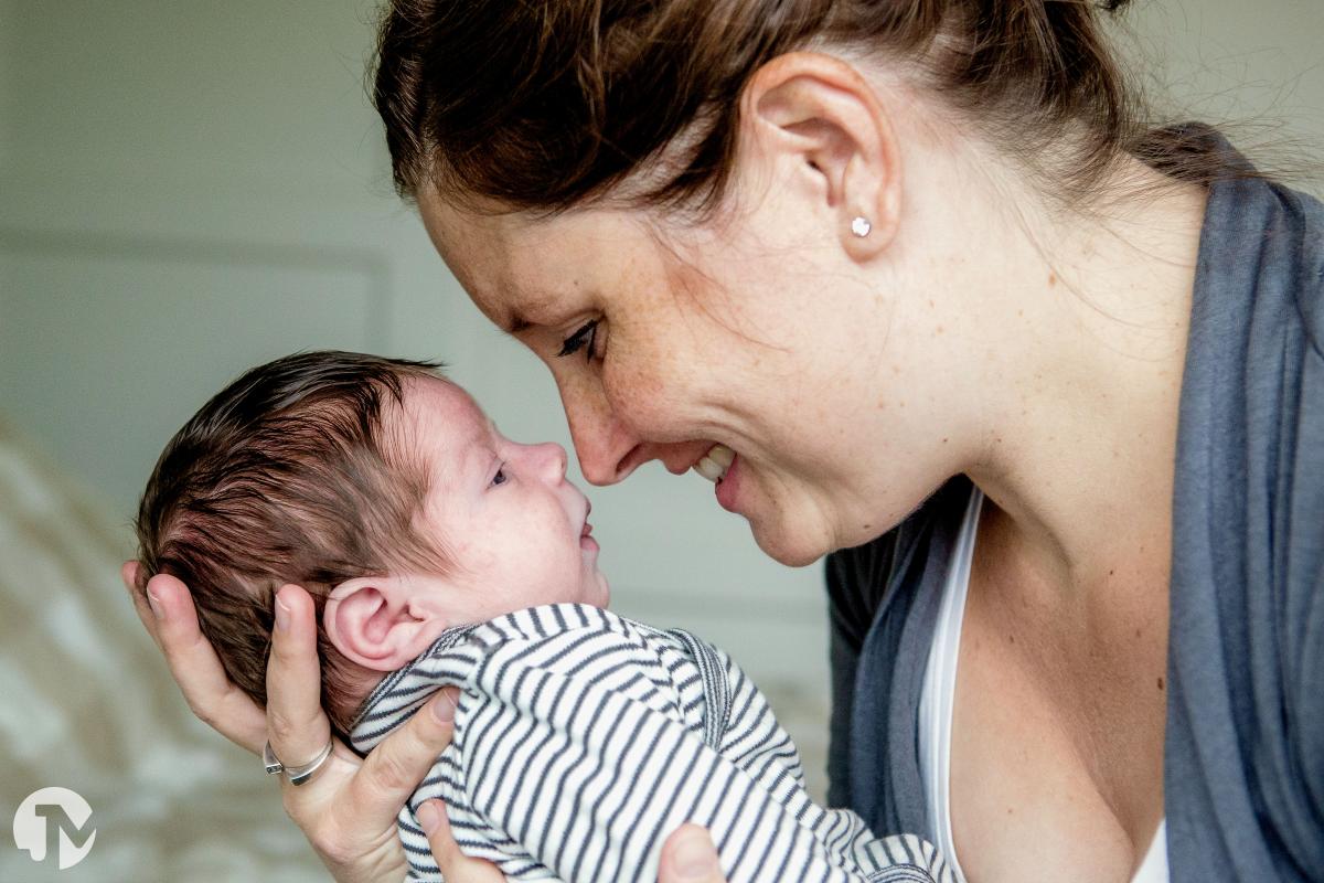 Moeder knuffelt liefdevol haar pasgeboren baby tijdens de fotoreportage.