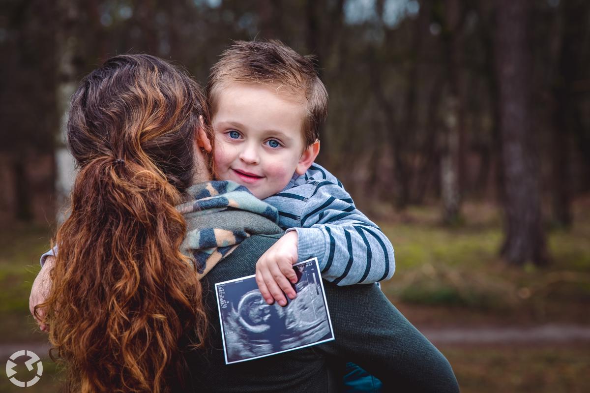 Jongetje buiten in de armen van vrouw met echo in zijn handen