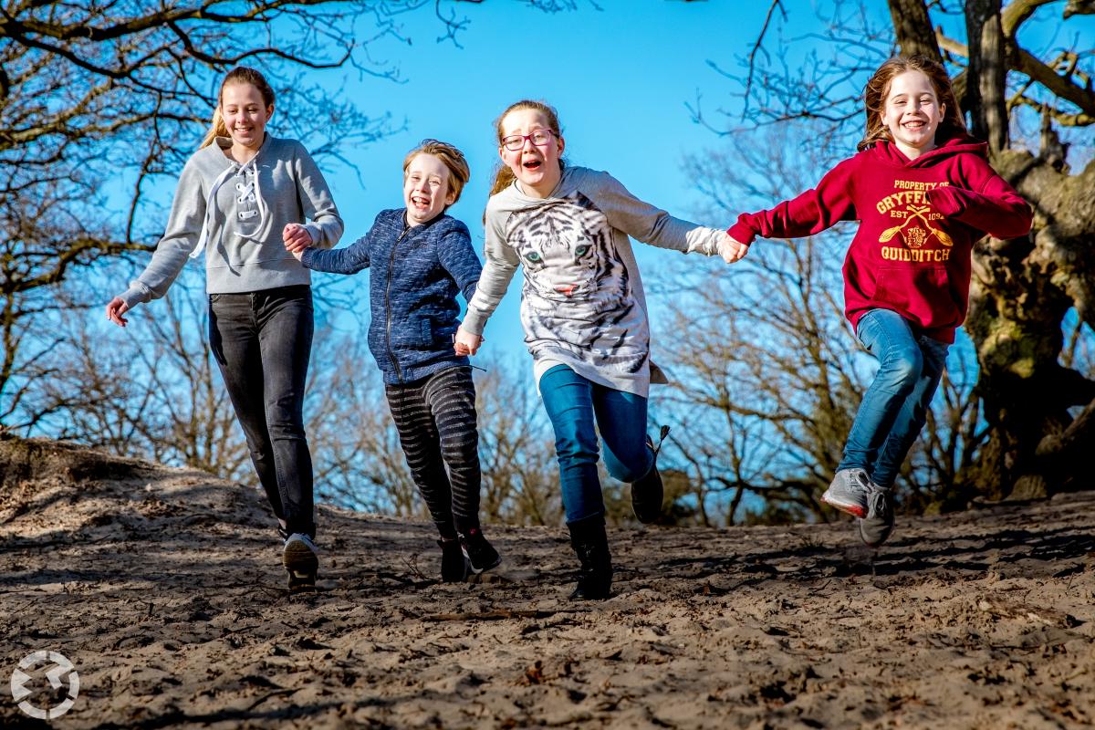 Vier kinderen rennen vrolijk een duinheuvel af 