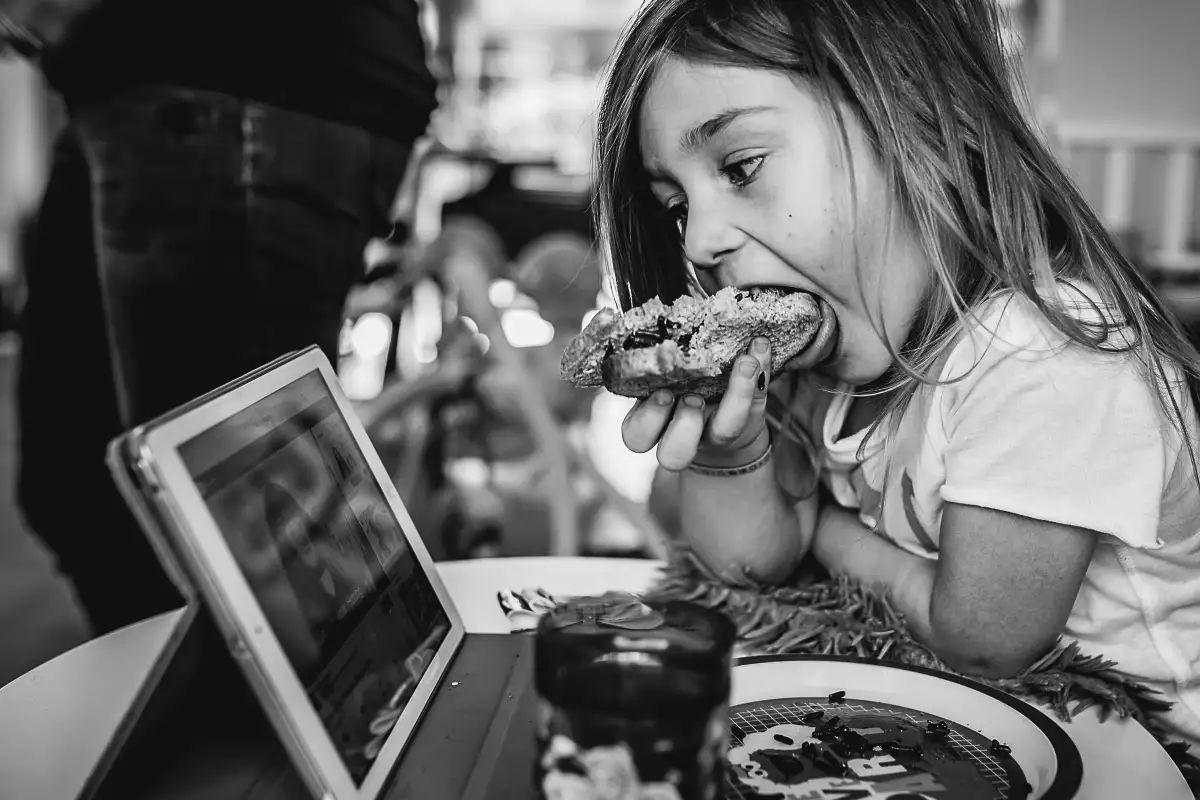 Meisje propt boterham in mond achter de iPad tijdens een fotoshoot.