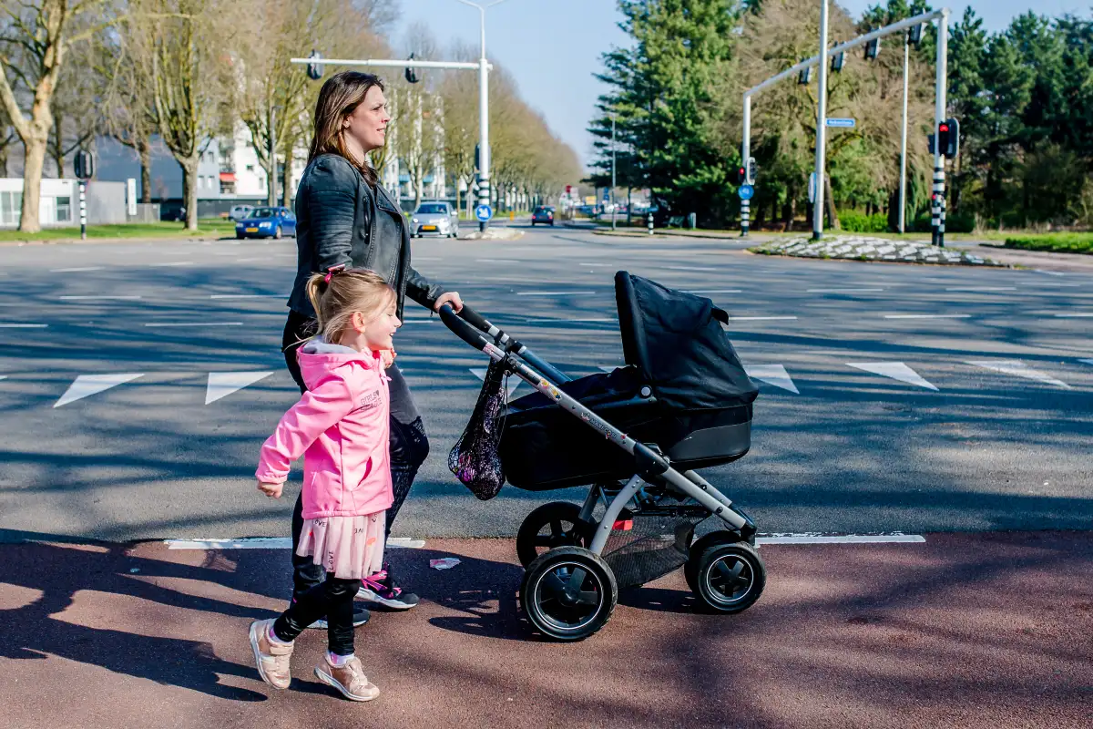 Moeder loopt met dochter en babywagen over de straat in Tilburg.