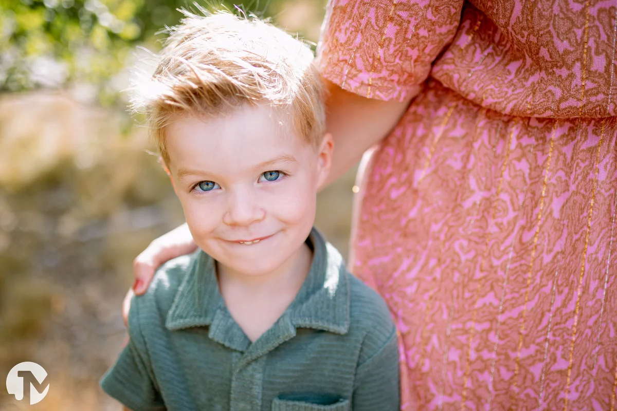 jongen met groen shirt hangt tegen zijn moeder met roze jurk tijdens de fotoshoot