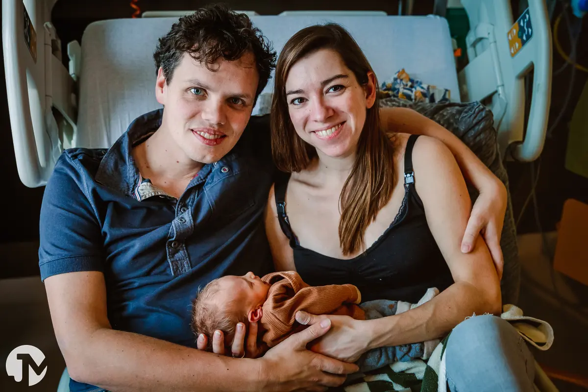 ouders poseren voor de foto op het ziekenhuisbed met hun pasgeboren baby