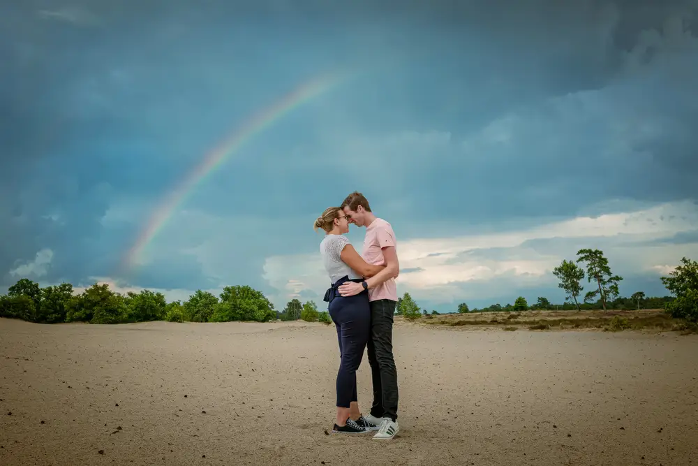 Verliefd stel poseert in de duinen met regenboog tijdens een loveshoot in Brabant.