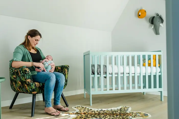 Moeder zit met haar baby op een stoel in de babykamer.