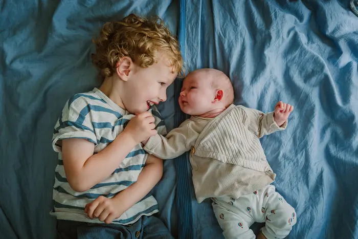 Broer met zijn baby zus kijken elkaar aan van bovenaf gefotografeerd.