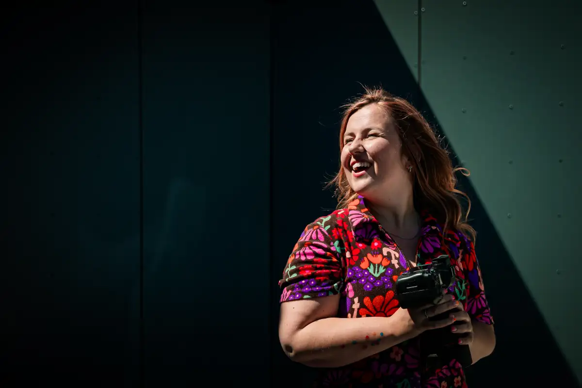 Fotograaf in het licht met camera in haar handen voor een donkere muur.