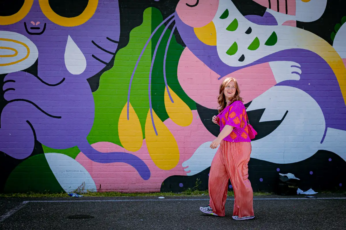 Kleurrijke vrouw loopt voor muur met beschildering.