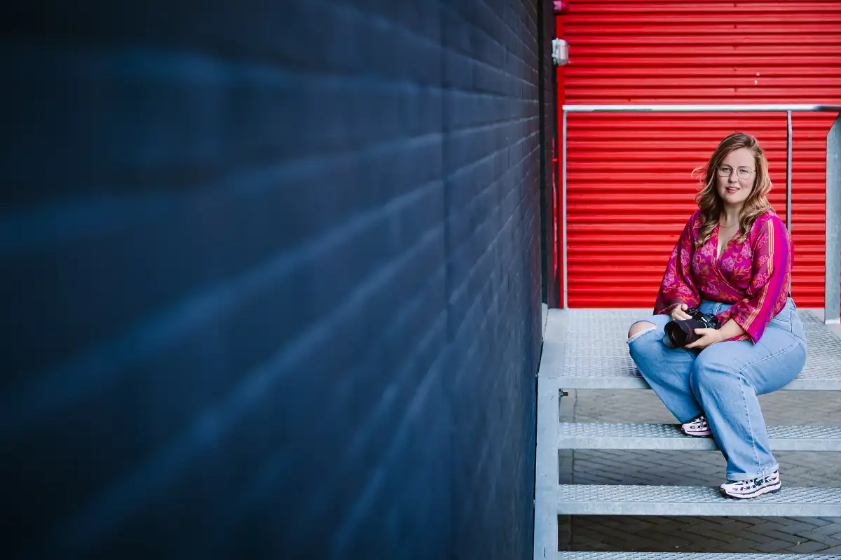 Fotograaf poseert op metalen trap bij zwarte en rode muur.