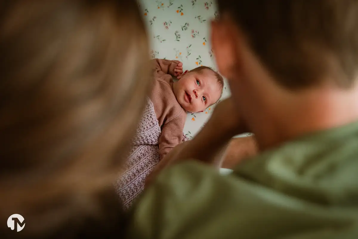 Ouders kijken naar hun baby dat in bed is gelegd tijdens een newborn fotoshoot.