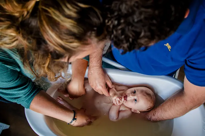 Newborn wordt in badje gedaan door beide ouders tijdens newbornshoot.