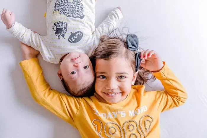 grote zus samen op bed met haar babyzusje.