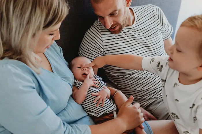 Jong gezin op bed met hun baby waarbij er aandacht voor de kleine is.