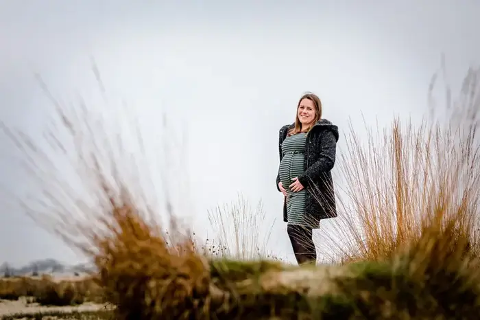 Zwangere vrouw poseert in duinen tussen hoog gras.