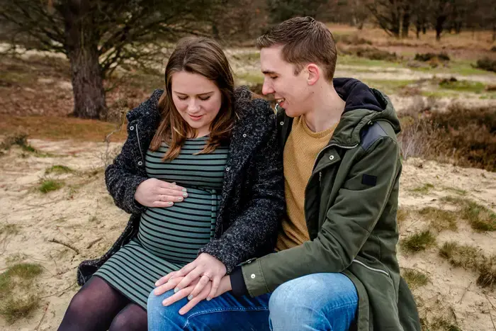 Man en vrouw zitten in het zand en hebben aandacht voor de zwangerebuik.