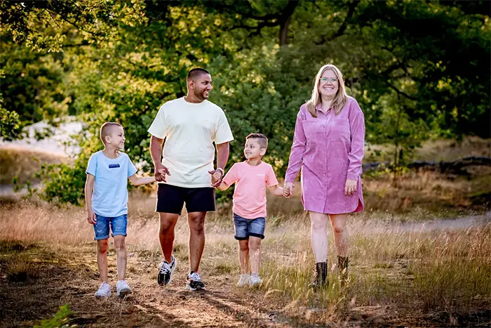 Gezin van vier wandelt hand in hand door een bos Loonse ne Drunense Duinen vastgelegd in warme portretfotografie met een natuurlijke spontane familieshoot sfeer