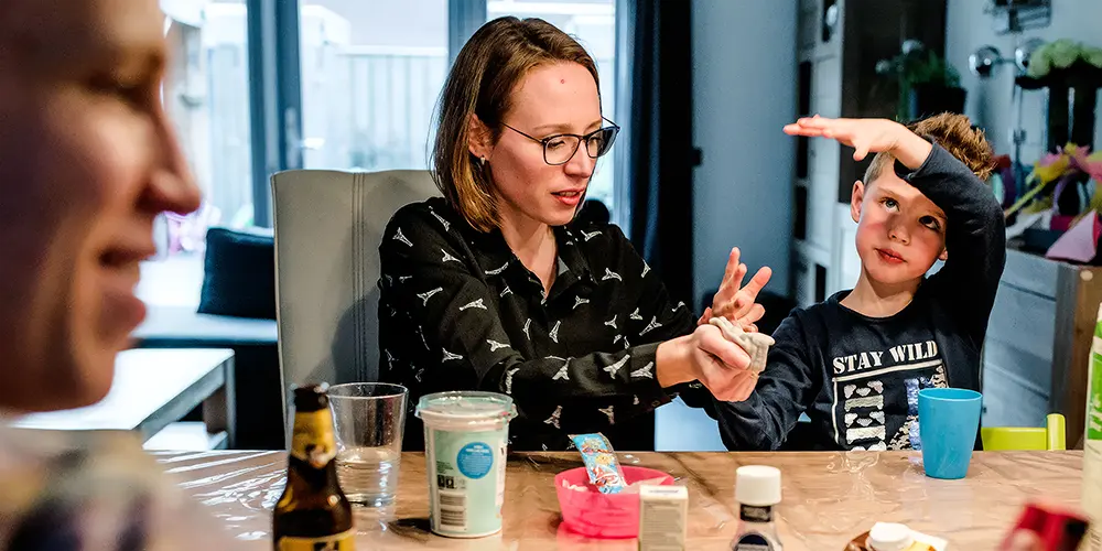 Zwangere vrouw in een roze jurk zit op rood gras en glimlacht rustig, vastgelegd in sfeervolle portretfotografie tijdens een natuurlijke zwangerschapsshoot