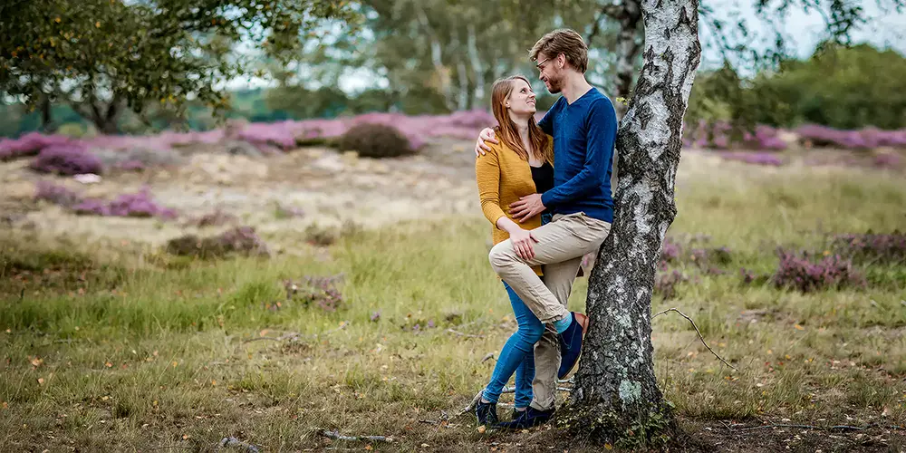 Zwangere vrouw in een roze jurk zit op rood gras en glimlacht rustig, vastgelegd in sfeervolle portretfotografie tijdens een natuurlijke zwangerschapsshoot